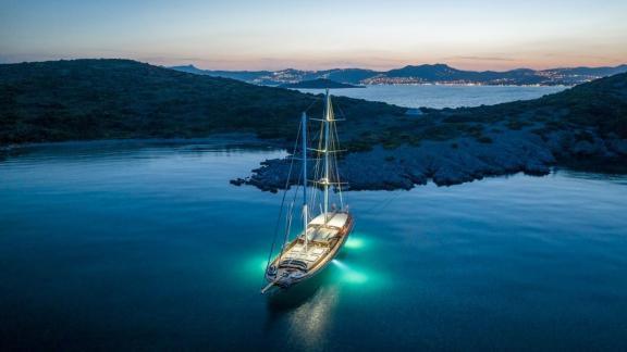 The gulet Bedia Sultan from Bodrum, illuminated and anchored in a quiet bay at sunset.