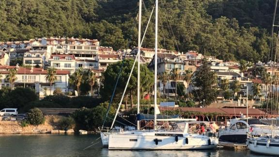 Segelyacht Triton 89 vor Anker in der Marina, umgeben von grüner Natur und luxuriösen Häusern.