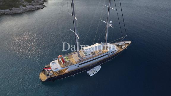 Luftaufnahme der prächtigen Dalmatino-Yacht vor Anker in türkisblauem Wasser nahe einer felsigen Küste.