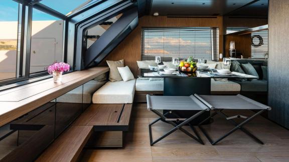 Motor yacht Kimani Bluegame BG74 features a refined dining and lounge area enclosed by expansive glass panels.