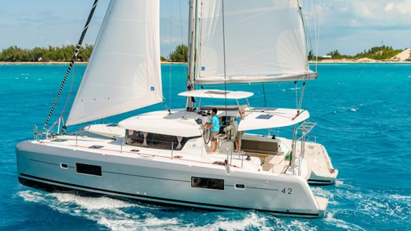 Aymeline catamaran sailing with crew on Croatia’s clear, turquoise waters, coastline in the background.