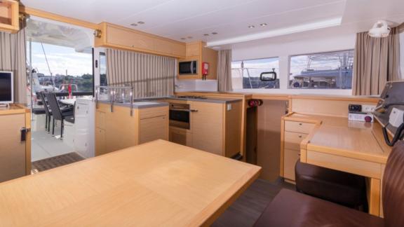 Bright galley and dining area with wooden furniture inside the Saelma Lagoon 450, equipped with modern appliances.