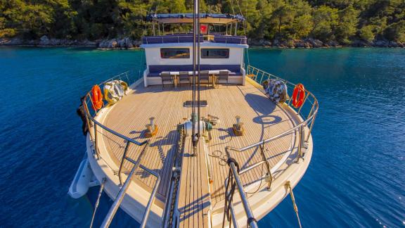 Blick auf das geräumige Deck der Gulet Buse mit 5 Kabinen, vor Anker in einer ruhigen, türkisfarbenen Bucht bei Bodrum.