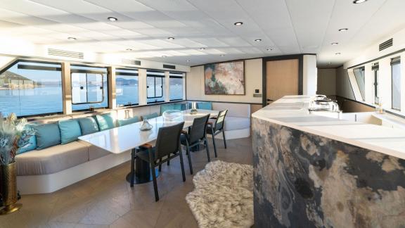 Yacht salon with a modern decor, featuring a large seating area and dining table, with a sea view.