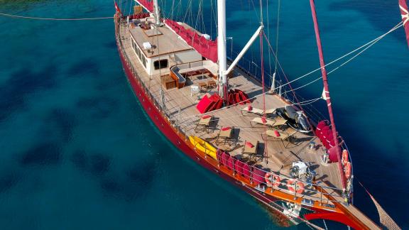 Eine luxuriöse Segelyacht mit rotem Segel auf klarem, blauem Wasser, ausgestattet mit Liegestühlen und Essbereich