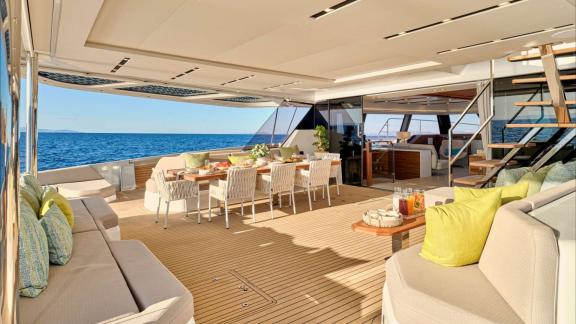 Large dining table with cushioned seats and sofas on the aft deck at sea.