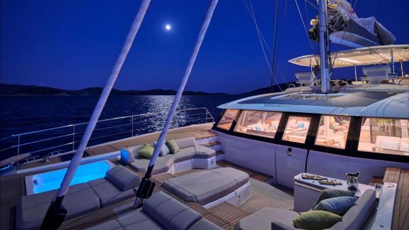 Anchored at night, Ad Astra glows with deck lights and a lit jacuzzi.
