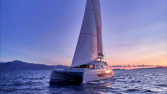 The Ad Astra catamaran sails near Lavrion during a vivid Mediterranean sunset.