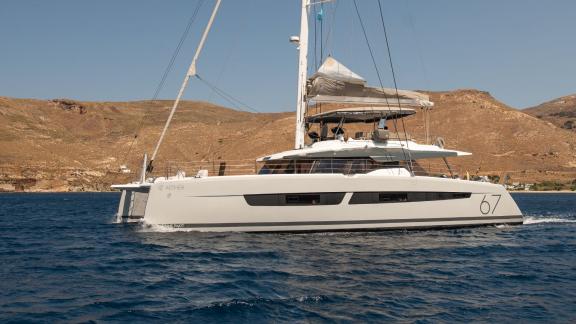 Yunanistan'da kayalık bir kıyı boyunca yelken açmış lüks Aether (Fountaine Pajot) katamaranı.