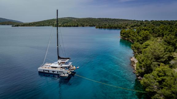 Agenda 55 catamaran is anchored in turquoise waters near Kastela surrounded by peaceful natural scenery.
