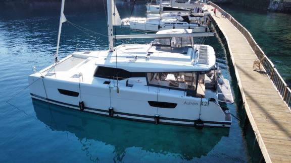 Катамаран Astrea 42 пришвартован к причалу и стоит на кристально чистой воде.