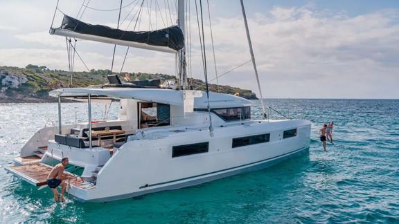 A catamaran is anchored in the bay and guests are swimming.