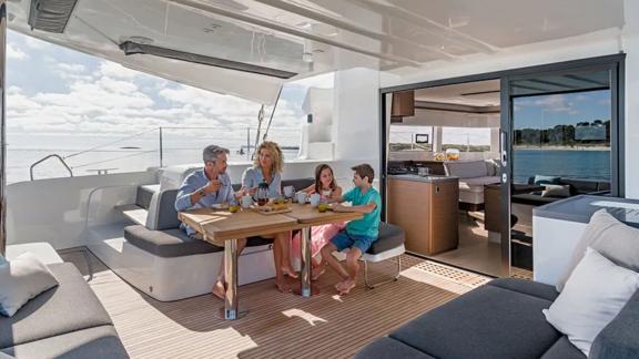 Children and their parents sit on the deck of the catamaran Alchera.