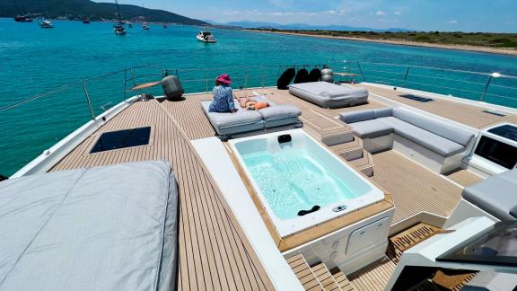 Catamaran sun deck with jacuzzi, surrounded by turquoise water and coastal scenery.