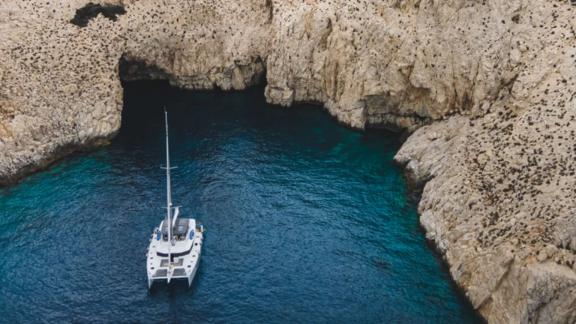 Allure catamaran for rent is anchored in a calm cove surrounded by cliffs.