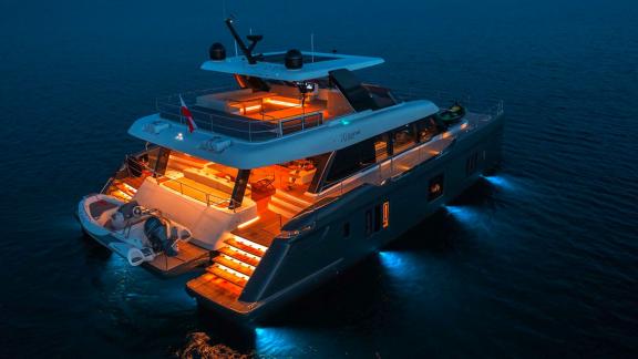 The Catamaran Alteya illuminates the sea at night with warm lights, creating a luxurious ambiance.