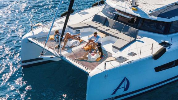 Four people relaxing on a catamaran's net, enjoying the sun and the sea.