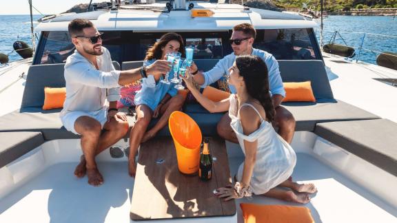 Four people raising their glasses and toasting on a catamaran's deck while enjoying the sun.