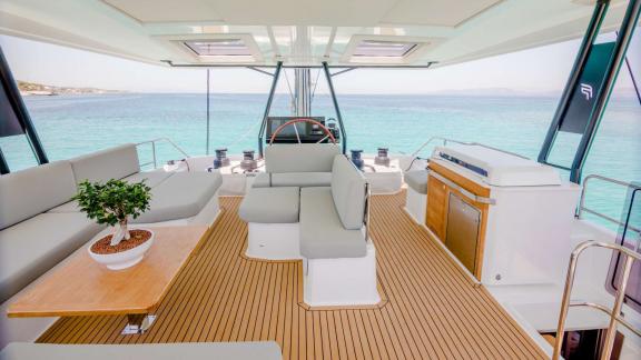 Flybridge mit hellem Sitzbereich, Holztisch, Steuerstand und Blick auf das Meer.