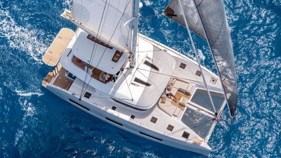 Lagoon 55 catamaran with full sails on deep blue waters, captured from above.