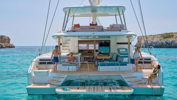 People relaxing on the deck of Lagoon 55 catamaran, anchored in crystal-clear waters.