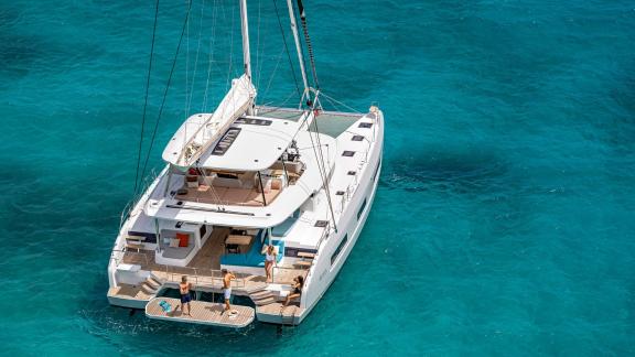 Lagoon 55 catamaran on turquoise waters, with people relaxing on the swim platform.