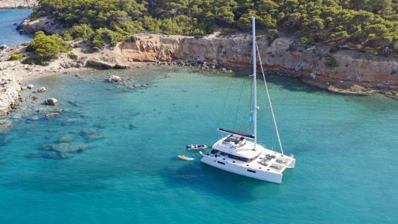 The Lagoon 560 anchored in a serene bay off the rocky coast of Athens, surrounded by clear turquoise waters.