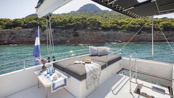 The flybridge of the Lagoon 560 in Athens offers a comfortable sunbed with views of the green coastline and clear waters