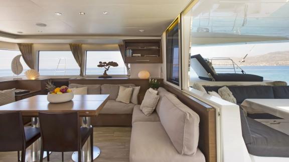 The bright salon of the Lagoon 560 in Athens with comfortable sofas and direct access to the elegant outdoor area with s