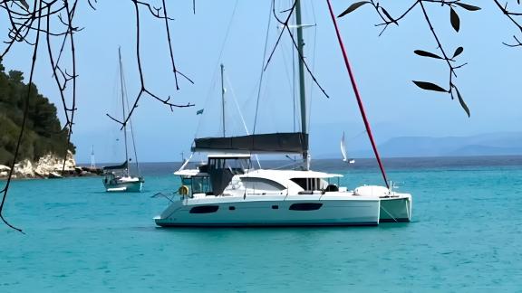 The catamaran Cecilia is seen anchored in a calm bay surrounded by lush greenery.