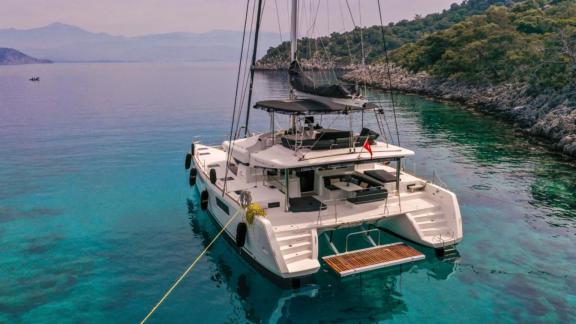 Der Katamaran Daphne mit 4 Kabinen, vor Anker in klarem Wasser nahe einer bewaldeten Küste in Fethiye.