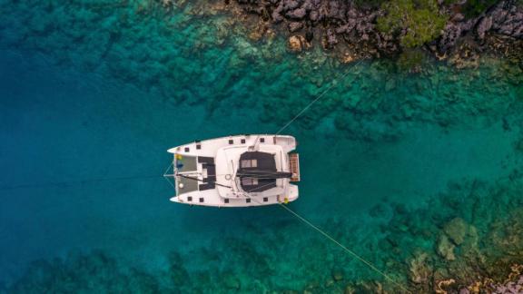 Der Katamaran Daphne liegt in einer geschützten Bucht mit klarem, türkisfarbenem Wasser und felsiger Küste vor Anker.