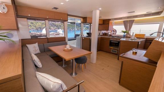 Open living area with dining table and fully equipped kitchen on the Daphne catamaran, overlooking the sea.