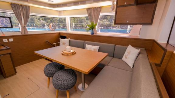 Inviting dining nook with cushioned seating and pillows in the salon of the Daphne catamaran, overlooking the sea.