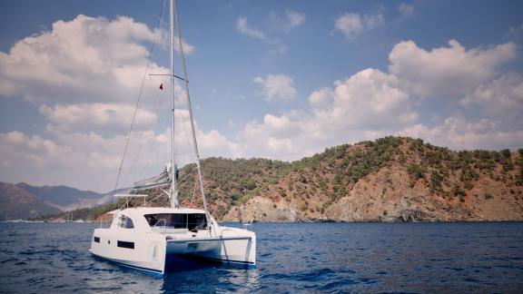 The catamaran Derya sails calmly on the water with a scenic natural backdrop.