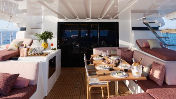 The aft deck of Dream catamaran features a dining table, pink-toned cushions, and a sea view.