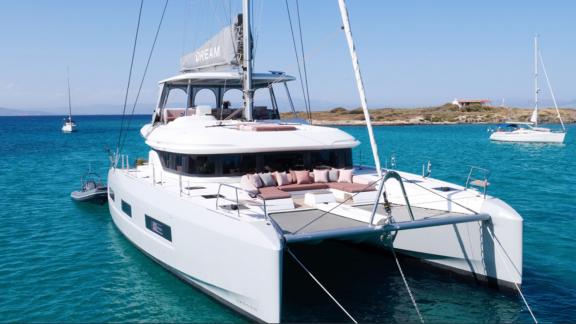 Dream catamaran rests on turquoise waters, its bow deck lined with cozy cushions.