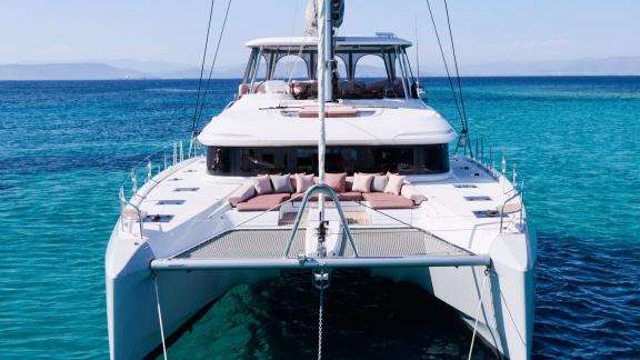 Dream catamaran rests on turquoise waters, its bow adorned with soft sunbeds.