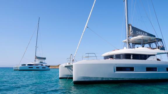 Dream catamaran lies anchored in clear waters beside another yacht near Athens.