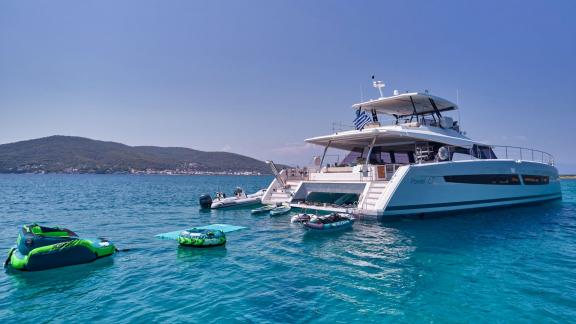 Fountaine Pajot Katamaran mit aufblasbarem Wasserspielzeug im türkisfarbenen Wasser vor Anker.