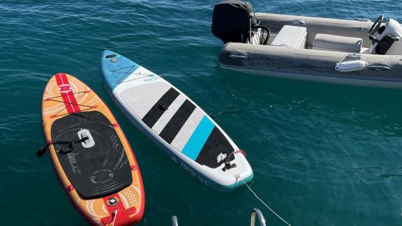 Zwei Paddleboards und ein Beiboot schwimmen neben dem Katamaran im klaren blauen Wasser, bereit für Abenteuer.