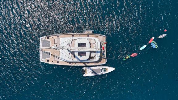 The Genny catamaran with tender boat and watersports gear, resting on calm, blue waters.