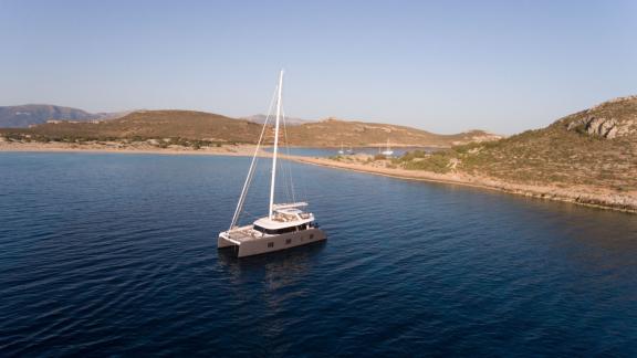 The Genny catamaran anchored in a secluded, serene bay with gentle hills in the background.