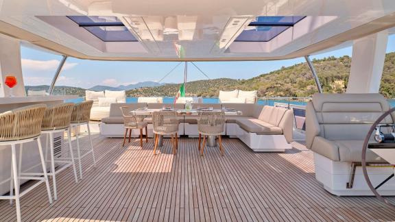 Elegant dining and bar area on the upper deck of the Genny catamaran, offering panoramic views of the surrounding landsc