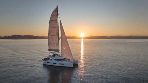 Der Katamaran Happy segelt bei Sonnenuntergang vor Athen und bietet eine ruhige, elegante Szenerie.