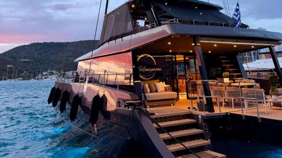 Der Katamaran Honeymoon liegt im Hafen von Lavrion vor Anker und zeigt sein beleuchtetes, luxuriöses Achterdeck.
