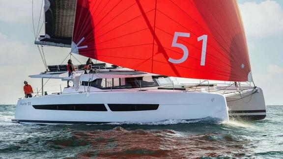 The catamaran Kebisiks speeds through waves off Athens with a bold red sail.