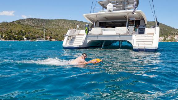 A man swimming beside the catamaran Kimata in the clear blue waters of a tranquil bay.