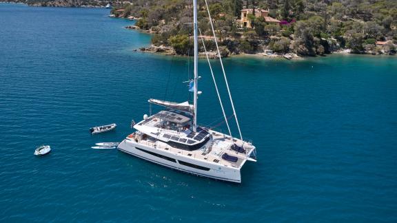 The catamaran Kimata anchored in a tranquil bay with clear blue water and a green coastline.