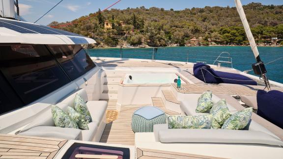 Cozy seating and a hot tub on the sun deck of the catamaran near a coastline.